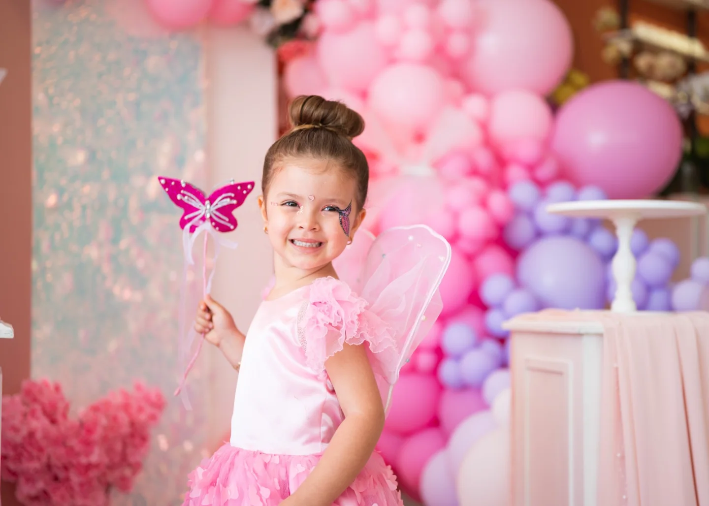 Girl in a pink dress in front of a pink balloon and butterfly backdrop