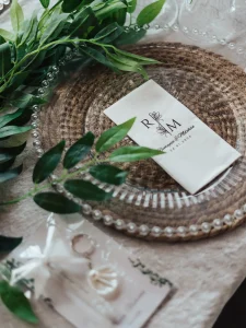 Engagement dinner place card with monogram on a glass charger plate and greenery