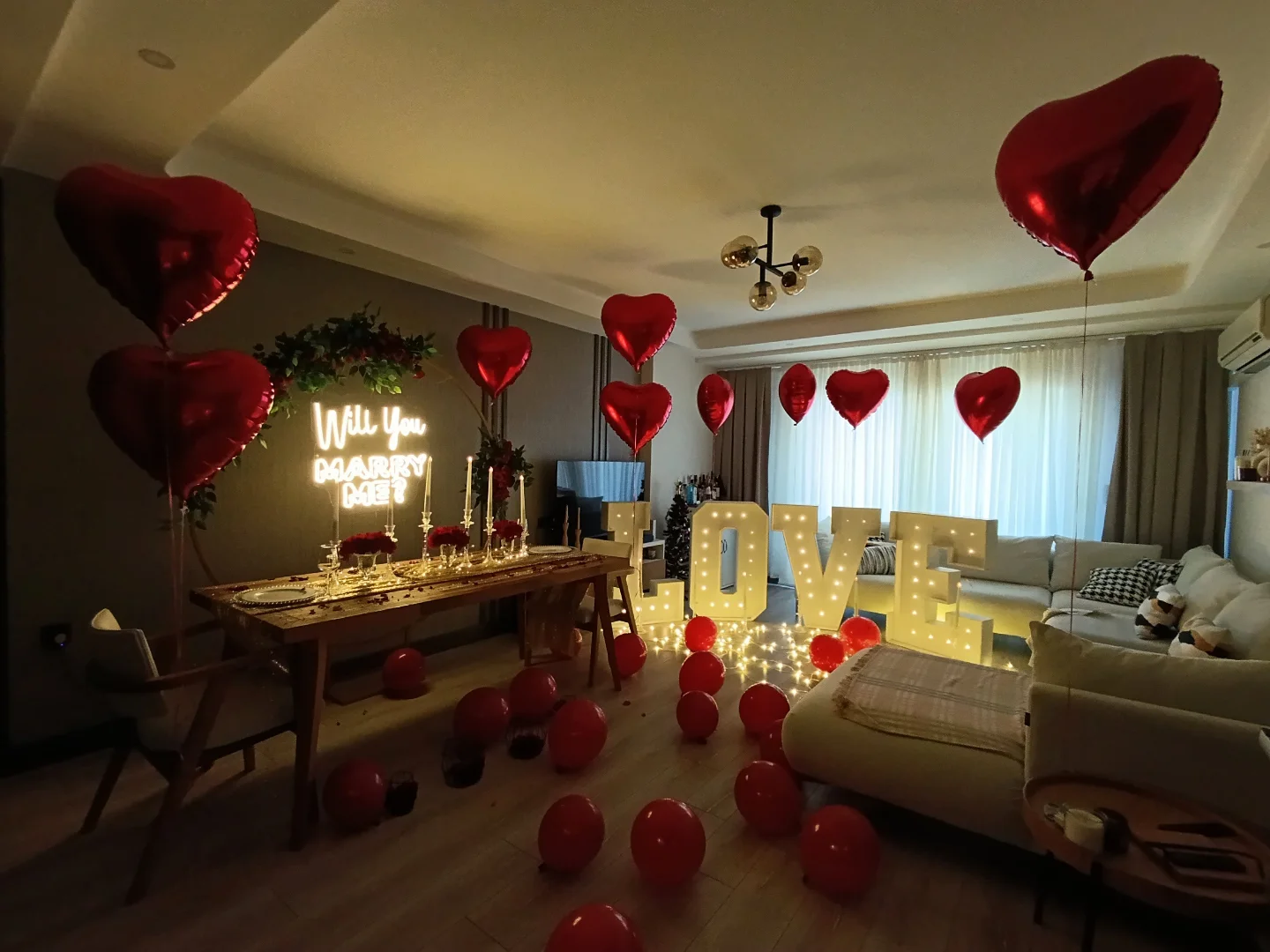 Romantic anniversary room decoration with red heart balloons, neon sign and candles