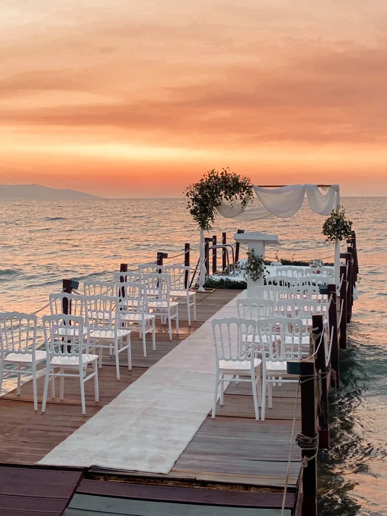 Sunset beach wedding setup with white chairs on a pier in Kusadasi