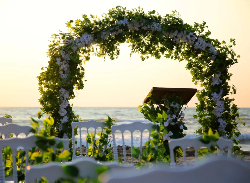 Wedding planner Turkey beach ceremony with floral arch, wooden lectern and white chairs at sunset