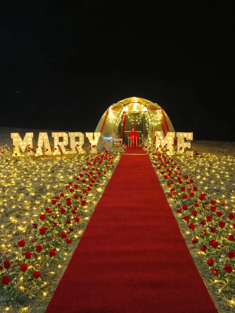 Red carpet aisle leading to a lit Marry Me arch at a beach proposal